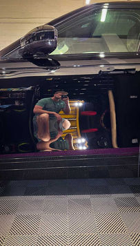 Shiny black car reflecting a person with a yellow chair and light.