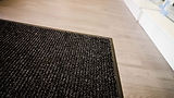 Close-up of a black doormat on a wooden floor.