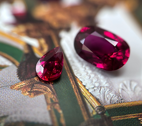 Two rubies of different sizes placed on green, yellow, and white fabric with a pattern resembling architecture