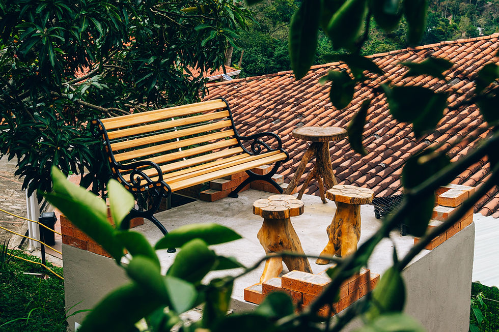 Banco de madera con mesas pequeñas en terraza con tejado rojo y vegetación.