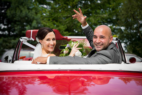 Newlyweds waving from a red convertible immediately after the ceremony in Canterbury.