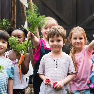 Happy preschool children holding vegetables in the garden
