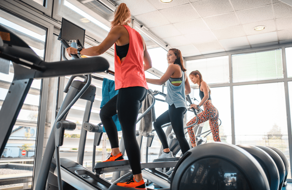 Three women exercise on elliptical machines in a bright gym. One wears orange shoes, another blue, and the third has leopard print leggings.
