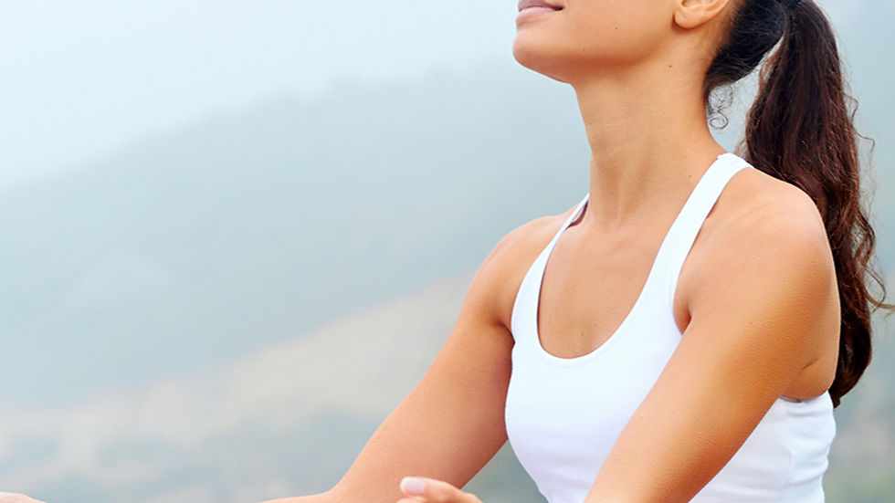 Woman meditating outdoors, wearing a white tank top. She's sitting cross-legged with eyes closed, looking peaceful. Misty background.