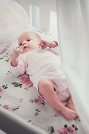 newborn baby lying on floral sheet in crib with white draped curtains. newborn lifestyle photography melbourne