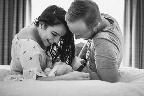 mother and father lying on their bed with newborn baby between them. Newborn lifestyle photography Melbourne