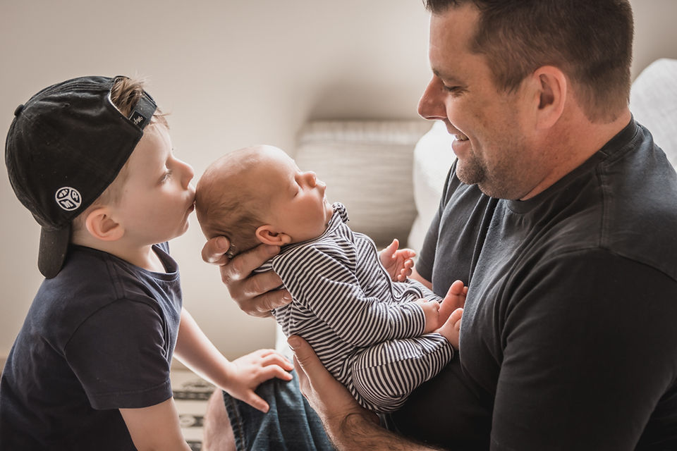 newborn lifestyle photoshoot melbourne - father holding newborn baby while toddler kisses the baby on the head