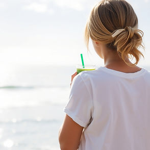 brownish blond haired pretty girl from behind holding green juice looking out to ocean.jpg