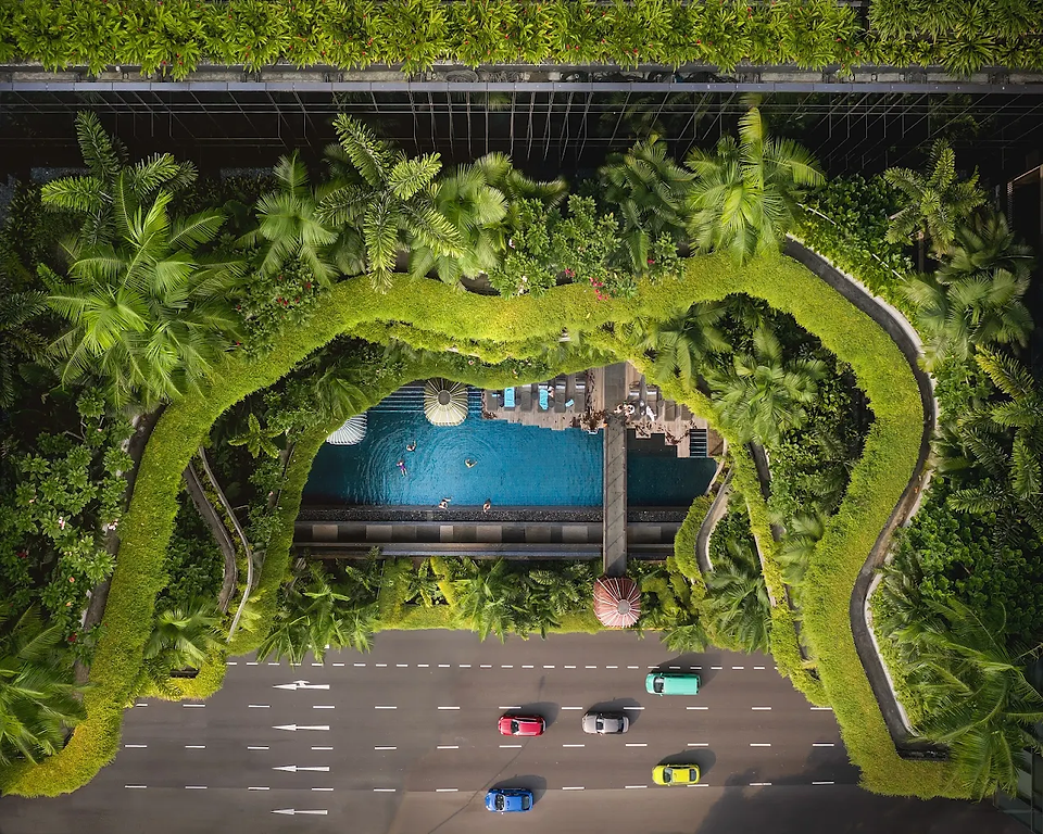  An aerial view of the Parkroyal Collection Pickering hotel in Singapore, showing its unique, lush green facade with a pool and a street below.
