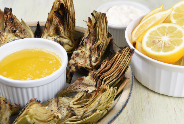 Grilled artichoke halves on a plate with dipping sauces.