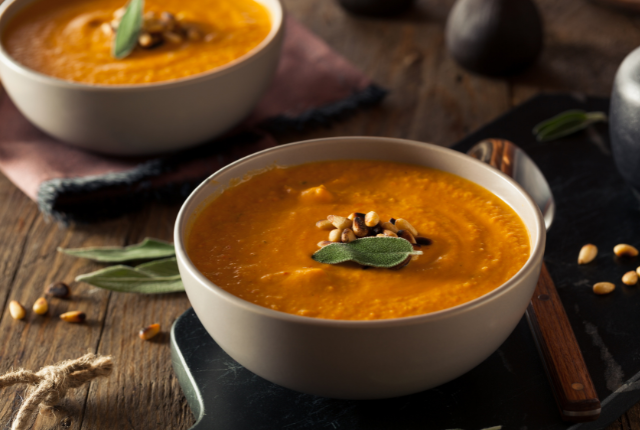 Two bowls of creamy carrot soup garnished with herbs.