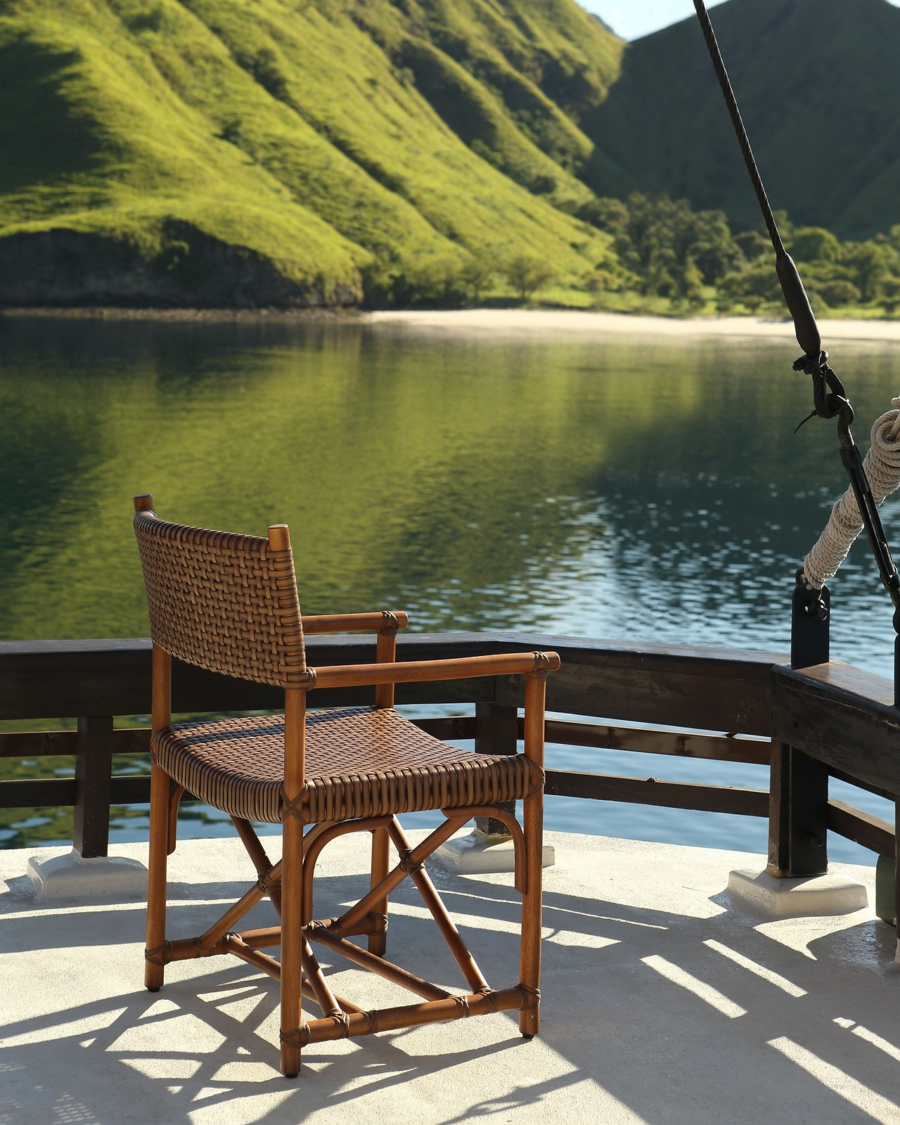 Wooden deck chair on Alila Purnama overlooking a tranquil bay and lush green hills, illustrating the harmony of sustainable design and natural surroundings.