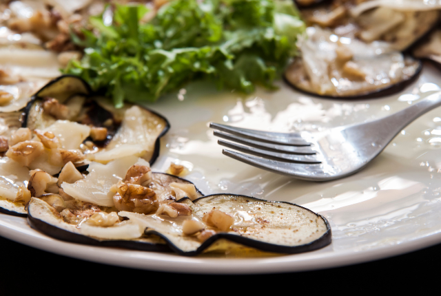 Eggplant carpaccio slices with toppings on a white plate.