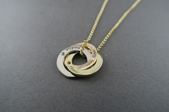 Collier formé de trois anneaux entrelacés en or 18k. Chaque anneau représente un des enfants avec le prénom gravé et la pierre de naissance sertie.