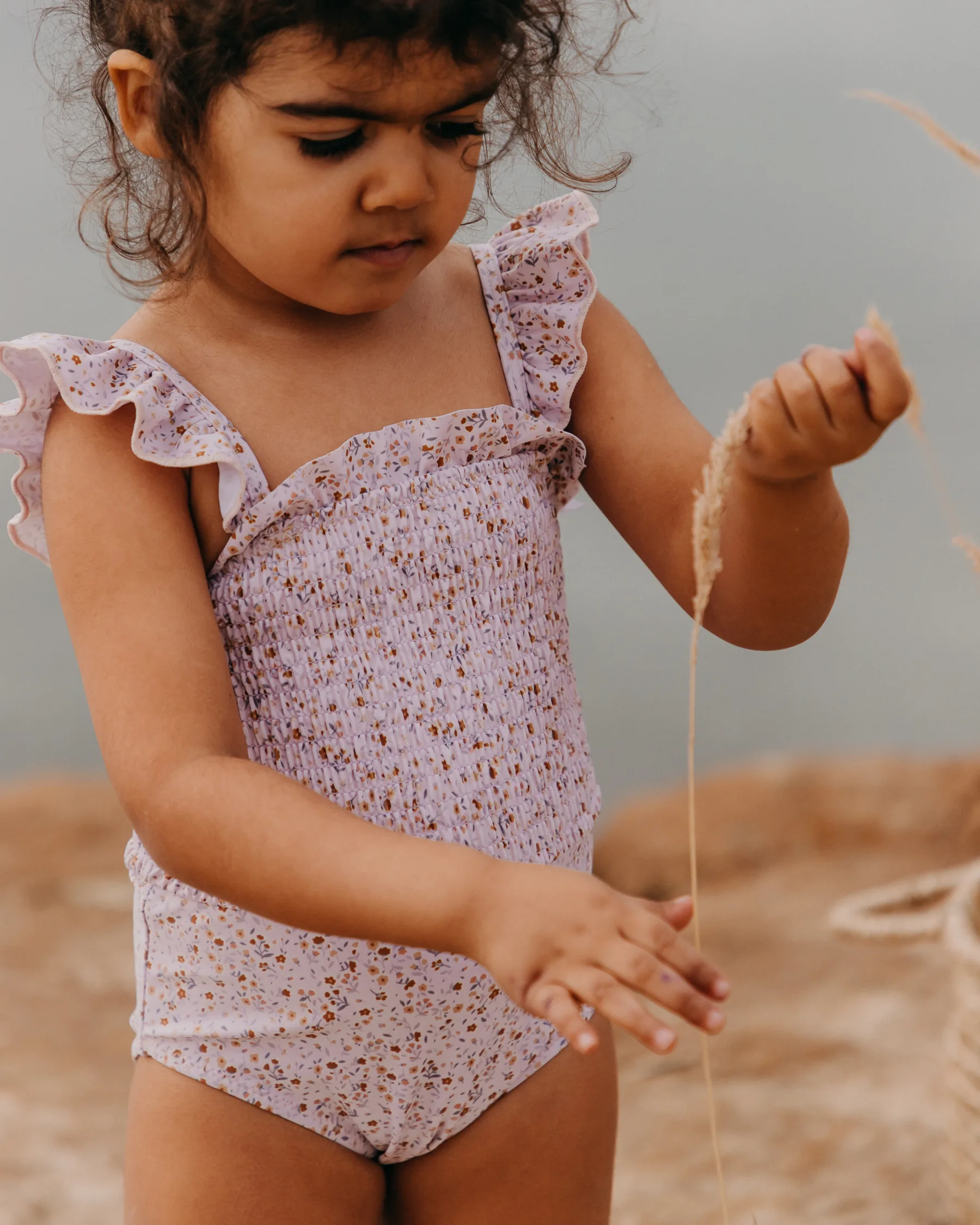 Girl playing with sand on the beach in floral swimsuit