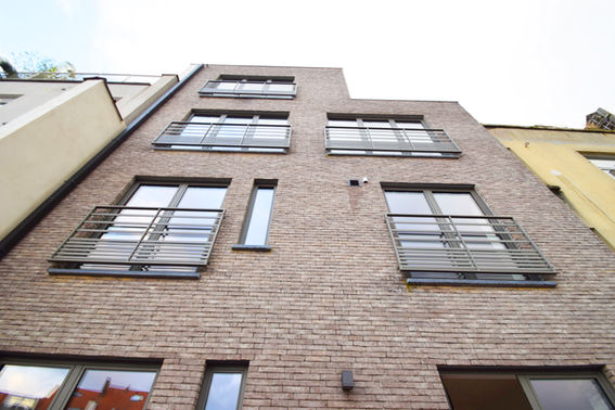 La façade arrière de la maison présente une esthétique moderne et élégante, caractérisée par l'utilisation de briques d'une teinte gris foncé. Ces briques confèrent à la façade une apparence solide et contemporaine, tout en ajoutant une touche de sobriété.

Les châssis, fenêtres et portes-fenêtres, sont d'une couleur anthracite, créant un contraste saisissant avec la teinte sombre des briques. L'alignement des châssis sur les différents étages offre une symétrie visuelle et une esthétique équilibrée à la façade. Le choix d'un nombre égal de divisions renforce cette symétrie, créant une géométrie régulière.

Les balustrades, également dans une teinte anthracite, complètent l'ensemble en ajoutant des éléments architecturaux cohérents. Ces balustrades contribuent à définir les espaces extérieurs tout en conservant la palette de couleurs moderne et harmonieuse.

Dans l'ensemble, la combinaison de la brique grise foncée, des châssis anthracite et des balustrades crée une façade arrière élégante et contemporaine, mettant en valeur l'attention portée aux détails et à la symétrie dans la conception architecturale.