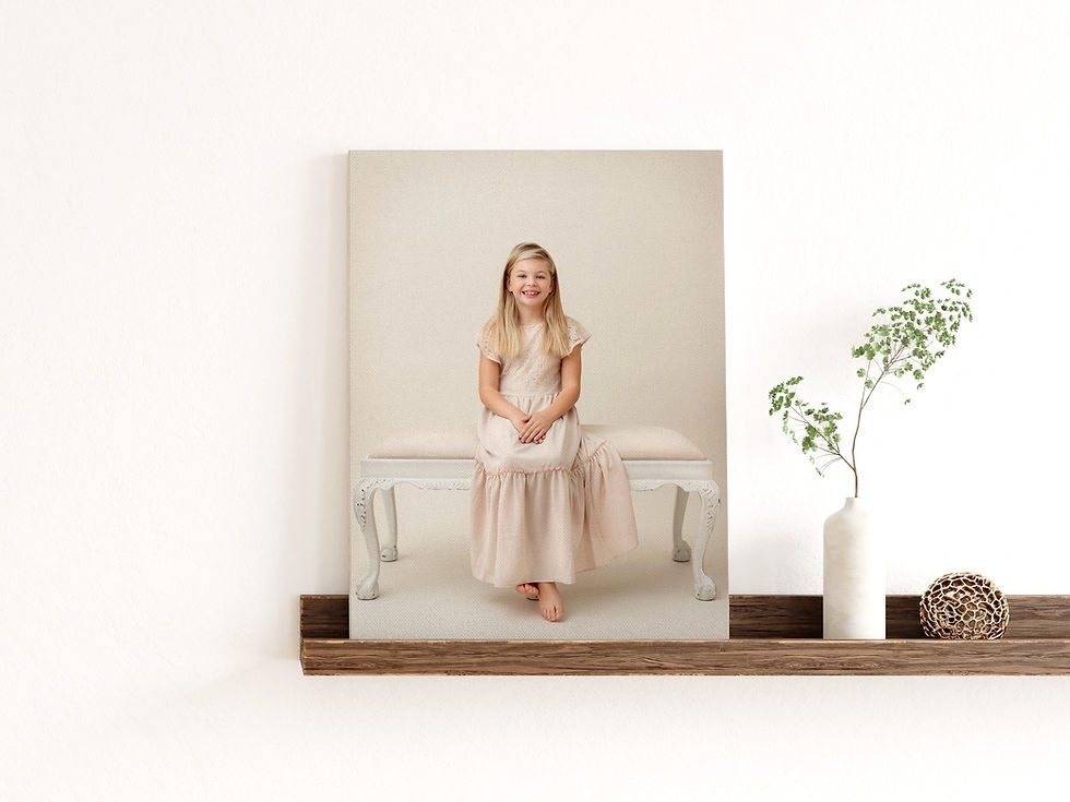 Canvas portrait on a shelf of a young girl with long blonde hair in a long cream dress sitting on a bench for a studio portrait.