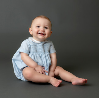 9 month old boy in a light blue heirloom bubble sitting on a dark gray backdrop for his sitter session.