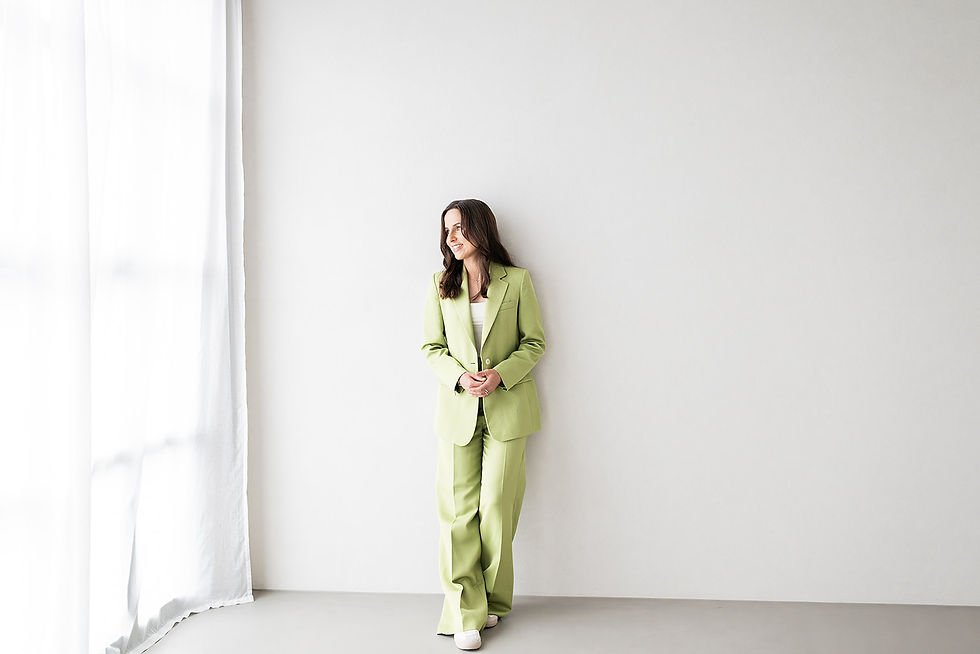 Frau im hellgrünen Anzug steht an einer weißen Wand in einem lichtdurchfluteten Raum