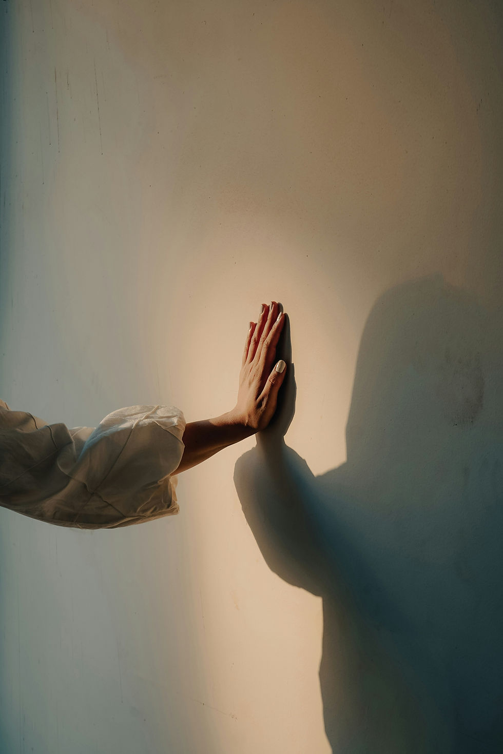 Hand, die eine Wand berührt; warmes Licht erzeugt einen weichen Schatten