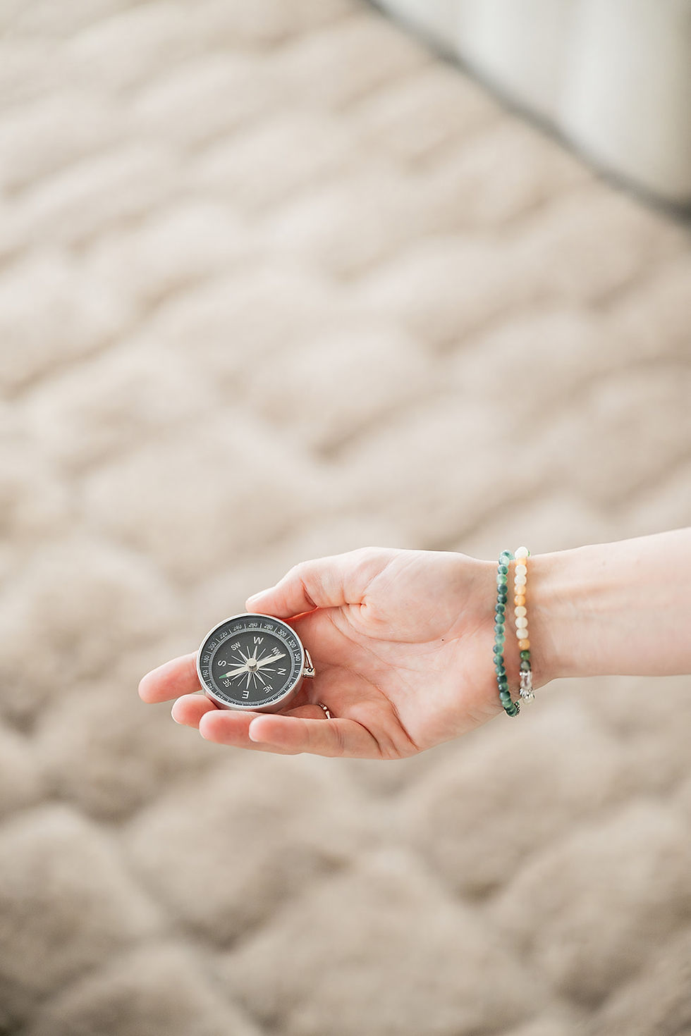 Hand hält einen Kompass über einem hellen, strukturierten Teppich