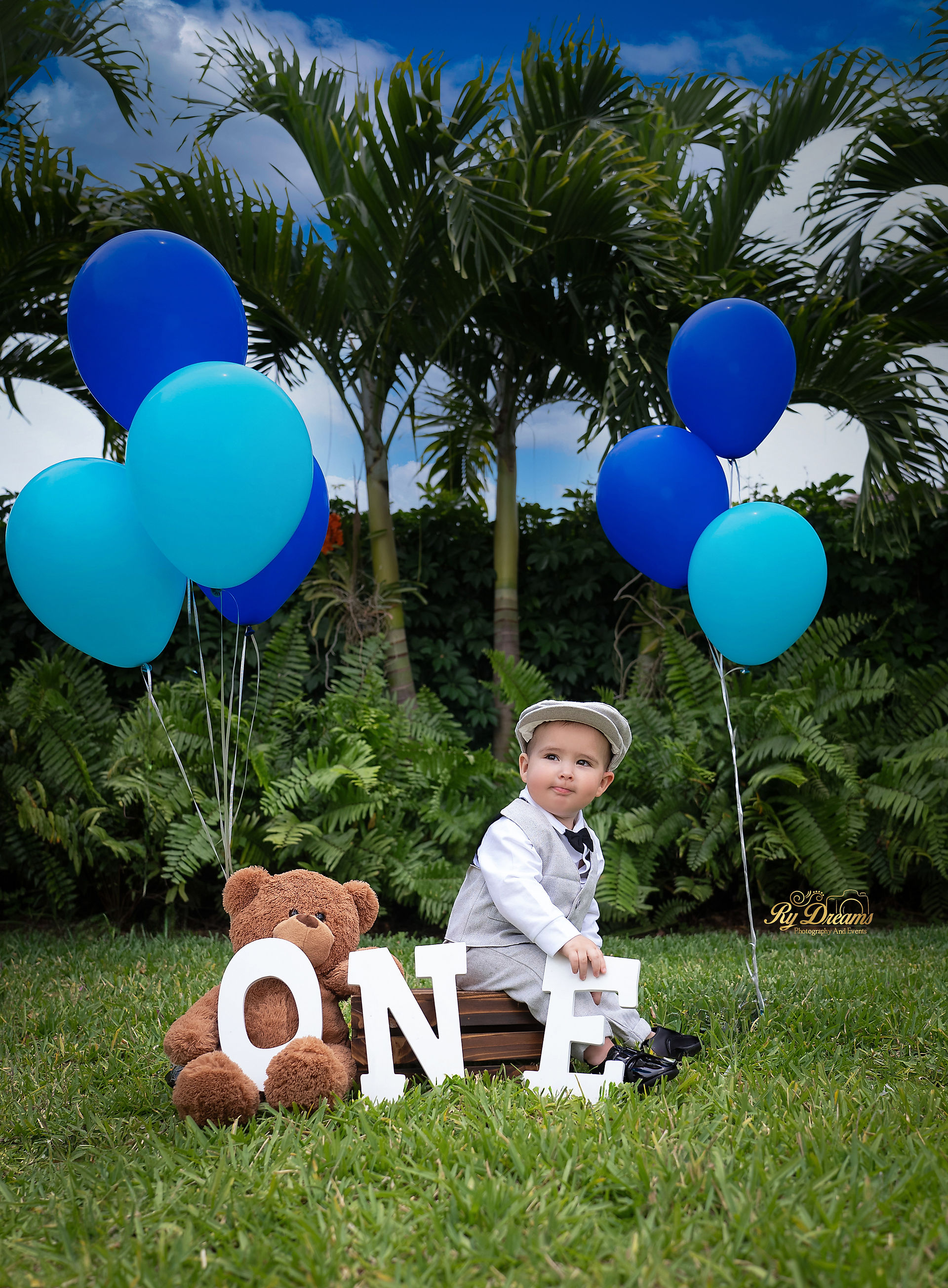 Un bebé niño con un traje gris rodeado de globos.