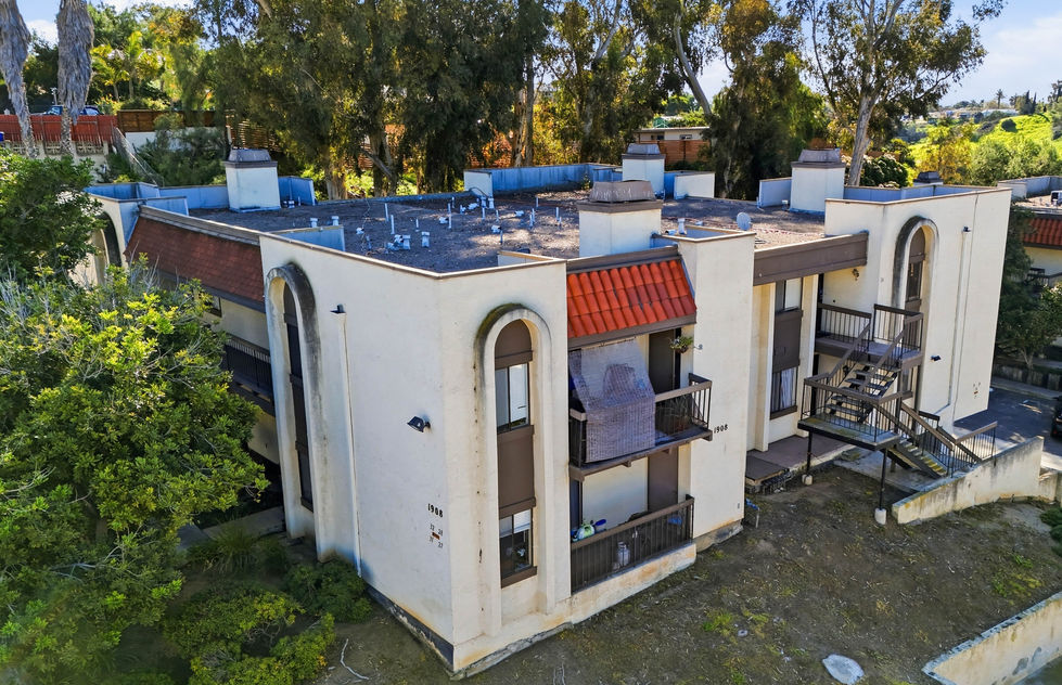 Exterior multi‑unit residential building with arched windows, red‑tile awnings, exterior staircases, balconies, and surrounding greenery.