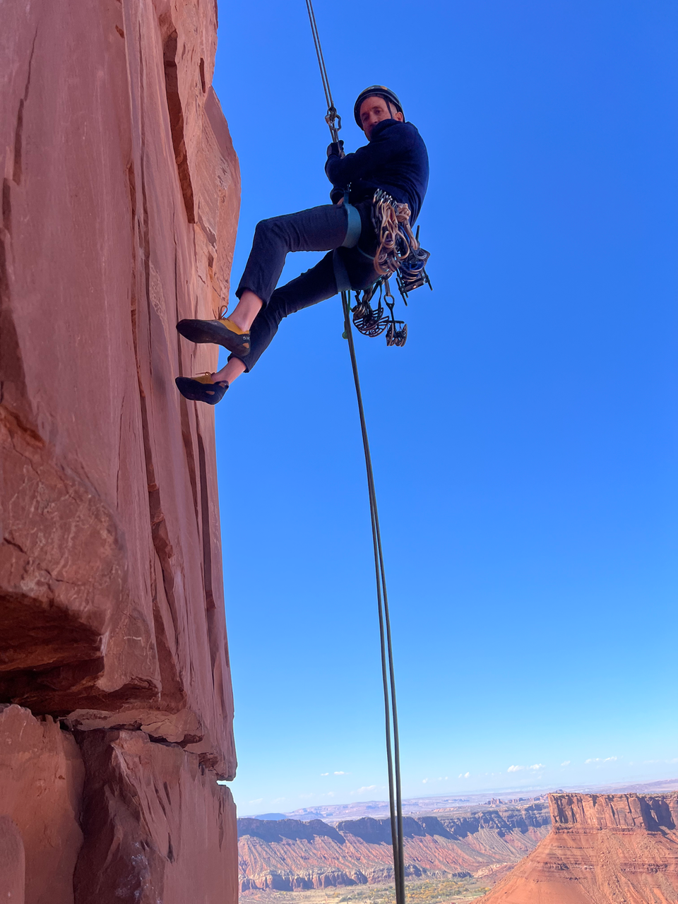 Rock climber rappelling down Castleton Tower, blue sky background, Moab Utah