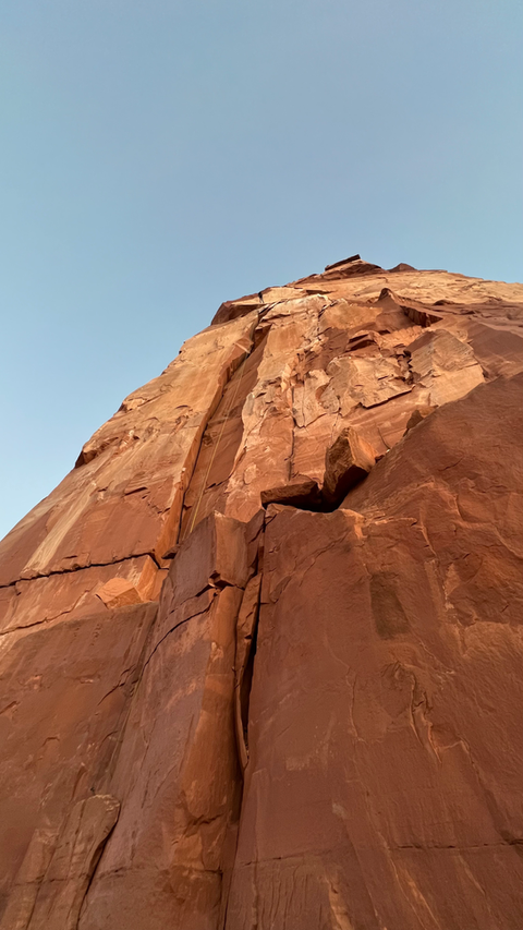 Red rock face of Castleton, looking upward, with clear sky backdrop; natural landscape view