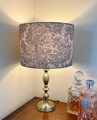 Zen Toile Marine Blue 25cm drum table lampshade on side table. Light on showing glow of light emitted.