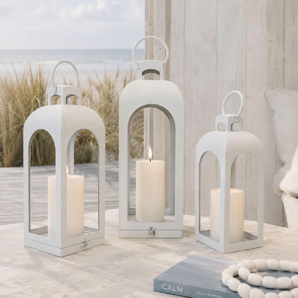 Off-white arched metal lanterns in three sizes styled with soft candlelight in a pale coastal interior.