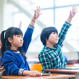 教室で手を挙げる子供たちの姿。学びへの意欲が感じられる瞬間を捉えています。