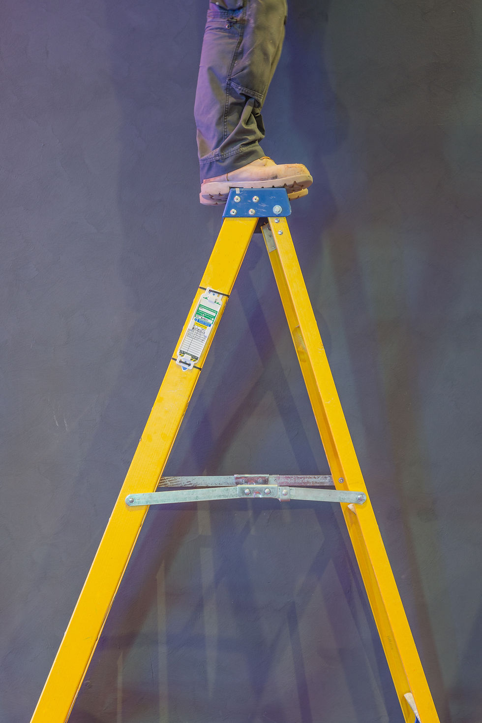 Construction worker standing dangerously on the top rung of a stepladder..jpg