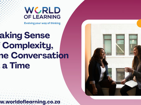 Making sense of complexity, one conversation at a time. Photo of two women sitting facing each other on a windowsill inside an office building. One has a laptop on her lap. They are smiling.