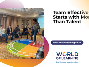 Team effectiveness starts with more than talent. Photo of Lesley standing on Insights Discovery model and discussing with a team seated around her in a meeting room.