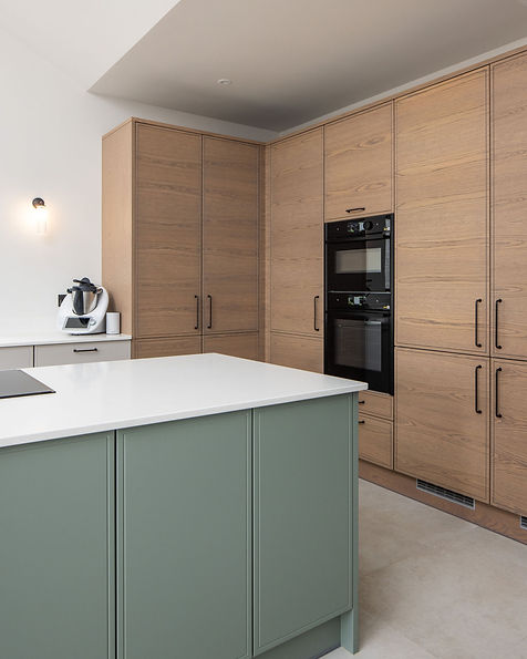 A modern Scandi design kitchen from the Stoneham Pitch range. Designed by Somerville kitchen studio for our client in St Lawrence, Jersey. With a light green island and tall Oak cabinetry housing Neff ovens