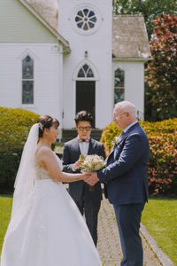 Bride and groom exchanging vows outside Minoru Chapel in Richmond, BC, with officiant standing between them.