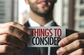 Man holds card reading "Things to Consider" in bold red and black text. Background is blurred, creating a focused, thoughtful mood.