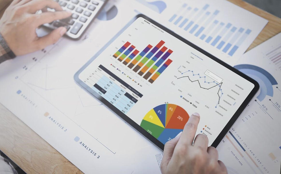 Tablet showing colorful charts and graphs on a desk with papers. A person uses a calculator and touches the tablet screen. Analytical setting.