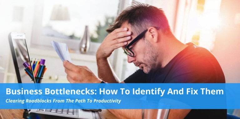 Man stressed at desk, holding a paper. Text: "Business Bottlenecks: How To Identify And Fix Them." Bright room with pens in holder.