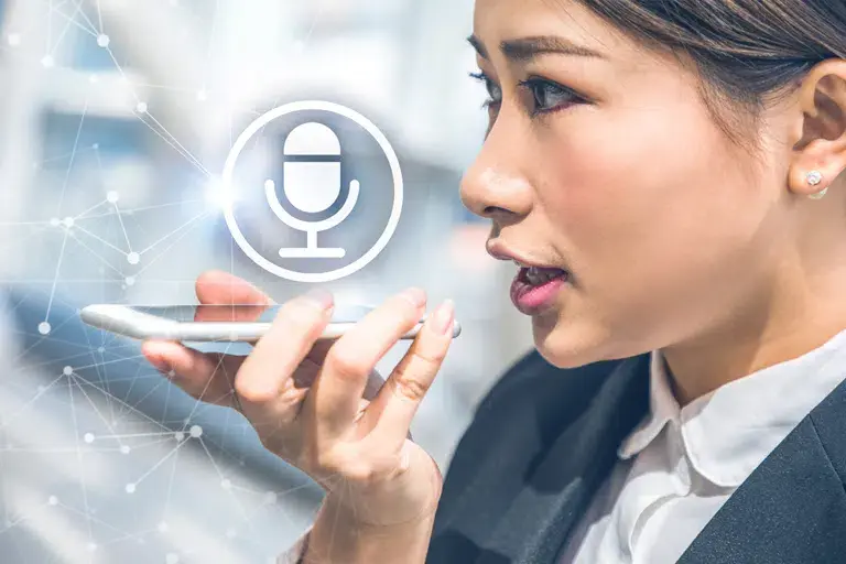 Woman using a smartphone voice command feature, with a microphone icon overlay. She's in an office, focused. Background has digital network lines.