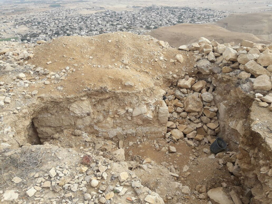 אתר חפירות ארכיאולוגיות, אדמה סלעית חשופה ועיר בנויה מרחוק.