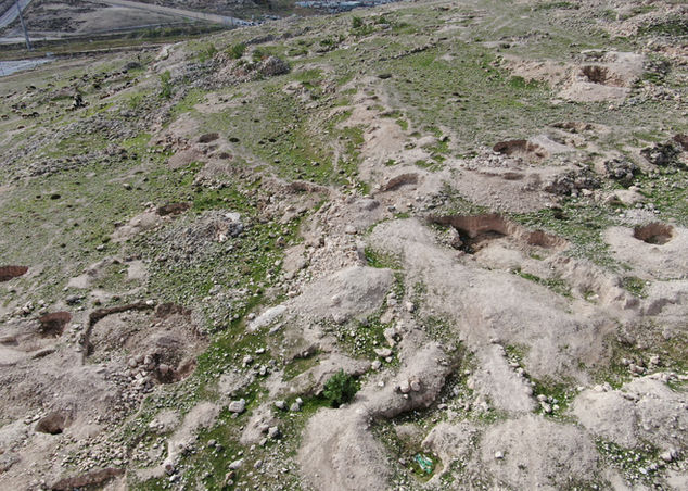 גבעות מחורצות עם חפירות ארכיאולוגיות וצמחייה דלילה, נוף אווירי.