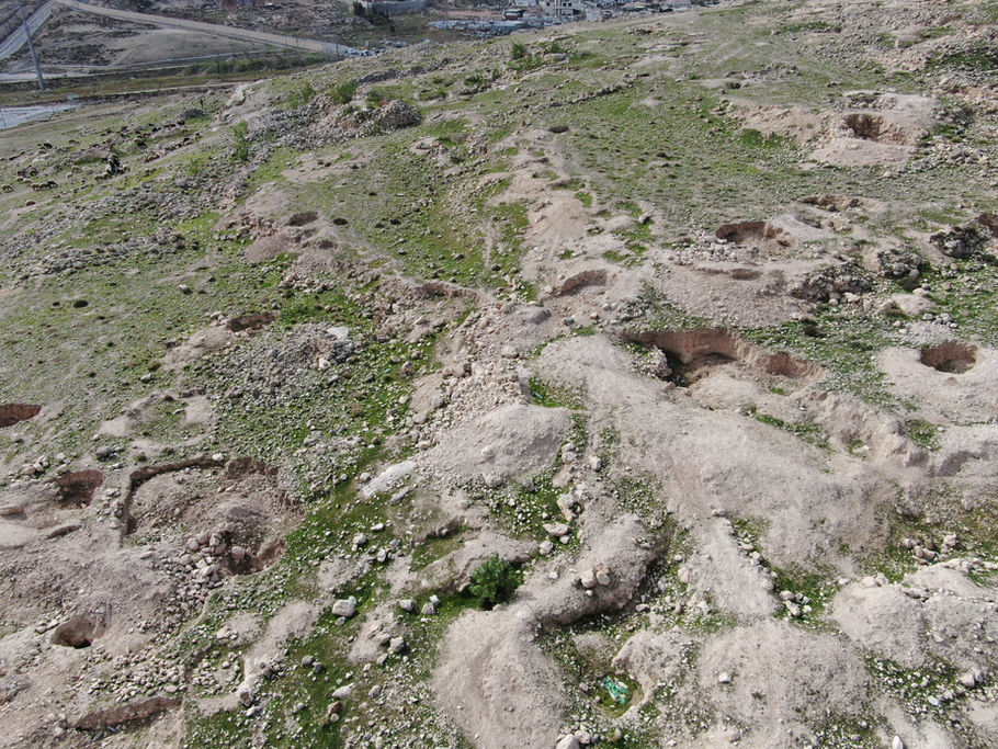 גבעות מחורצות עם חפירות ארכיאולוגיות וצמחייה דלילה, נוף אווירי.