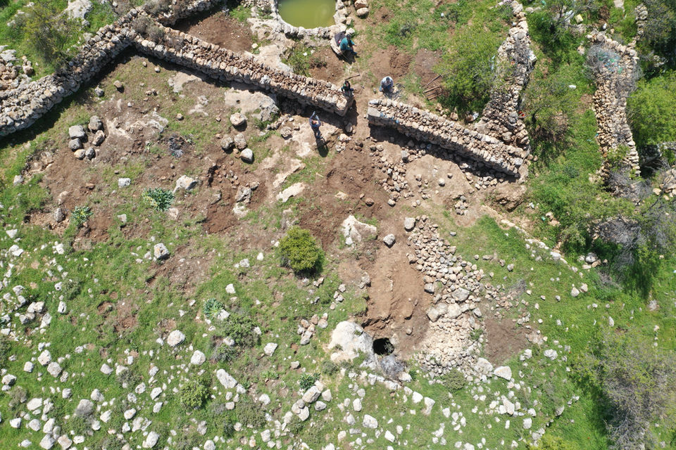 מראה אווירי של ארכיאולוגים המשפצים חומת אבן עתיקה בנוף ירוק.