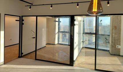 משרד מודרני עם קירות זכוכית, נוף לעיר, תאורה תלויה ומסגרות שחורות