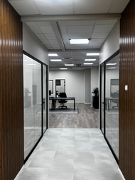 משרד עם קירות זכוכית, שולחנות עבודה, ותאורה לבנה. עיצוב מודרני משרדי.