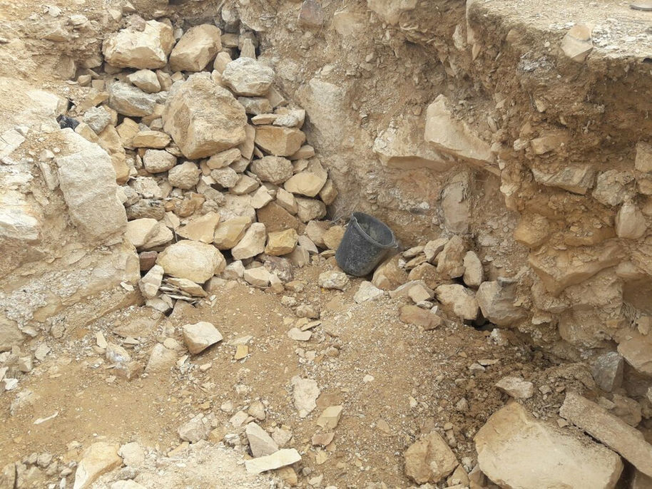 אתר חפירה עם אבנים גדולות, אדמה רופפת ודלי שחור.