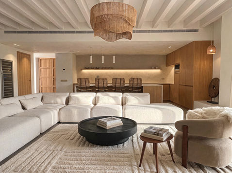 Open-plan living room and natural oak kitchen at Can Bella, a luxury townhouse in Muro, Mallorca, with a cream modular sofa, woven pendant and kitchen island.