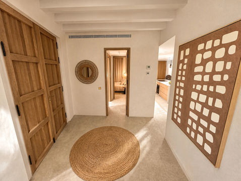 Main entrance hall of Can Bella, a luxury townhouse in Muro, Mallorca, with a wooden entrance door, circular woven rug, wall mirror and geometric artwork.
